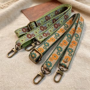 Könnte beinhalten: Drei dekorative Handtaschenriemen mit floralen Mustern. Die Riemen weisen grüne, braune und orangefarbene Blumen mit antiker Messingbeschlägen auf. Die Riemen sind mit einem floralen Muster versehen und eignen sich wahrscheinlich für Handtaschen oder Geldbörsen.