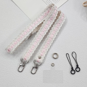 Op de afbeelding: Drie witte en roze kanten bandjes met zilveren metalen sluitingen en hardware. Twee zwarte lussen en twee zilveren ringen zijn ook inbegrepen. De bandjes hebben een delicaat, vrouwelijk ontwerp.