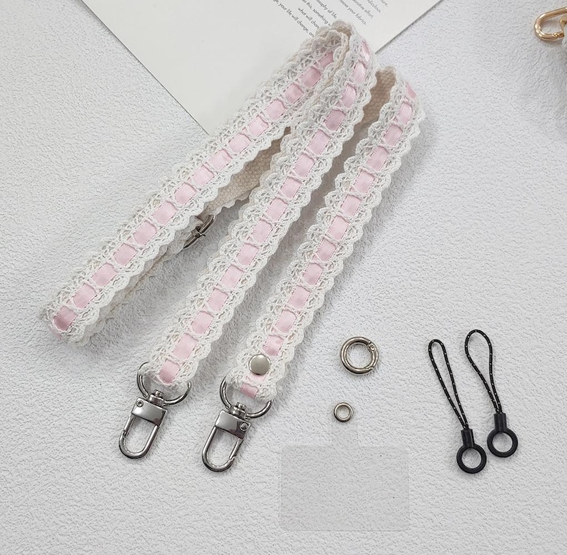 Op de afbeelding: Drie witte en roze kanten bandjes met zilveren metalen sluitingen en hardware. Twee zwarte lussen en twee zilveren ringen zijn ook inbegrepen. De bandjes hebben een delicaat, vrouwelijk ontwerp.