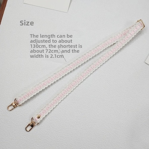 Op de afbeelding: Een witte en roze kanten band met goudkleurige metalen sluitingen. De lengte van de band is verstelbaar, tot 130 cm, met een minimale lengte van 72 cm. De band is 2,1 cm breed.