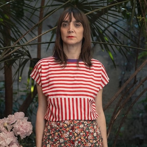 May include: A short-sleeved shirt with horizontal red and white stripes on the top half and vertical red and white stripes on the bottom half, paired with a dark-colored midi skirt featuring a dense floral pattern and a front button closure.