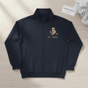 May include: Navy blue zip-up track jacket with a high collar and two front pockets. The jacket features a cartoon graphic on the chest and the text "ApexVisualArts Est. 2026" on a small white tag.