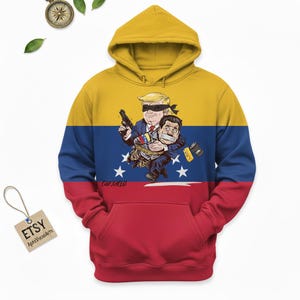 May include: A hooded sweatshirt with a yellow, blue, and red design, resembling a flag. The front features a cartoon illustration of two figures, one with a blindfold and gun, the other bound and gagged. The word "CAPTURED" is printed on the front.