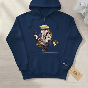 May include: Navy blue zip-up hoodie featuring a cartoon illustration. The graphic depicts a blindfolded figure holding a gun and another figure tied up. The illustration includes the text "CAPTURED".