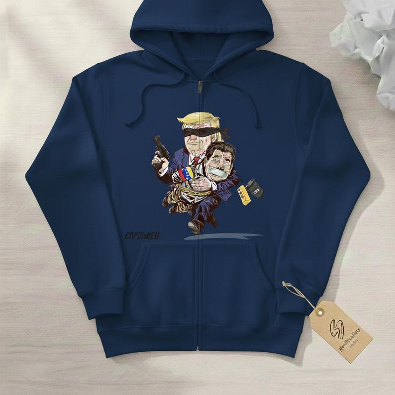 May include: Navy blue zip-up hoodie featuring a cartoon illustration. The graphic depicts a blindfolded figure holding a gun and another figure tied up. The illustration includes the text "CAPTURED".