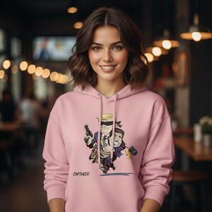 May include: A light pink hoodie with a cartoon illustration of two figures, one holding a gun and the other a briefcase. The word "CAPTURED" is printed below the illustration.