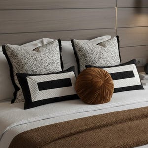 May include: A bed with decorative pillows. Two square pillows with black fringe and a textured black and white pattern. Two rectangular pillows with a black stripe and a white border. A round, brown velvet pillow.