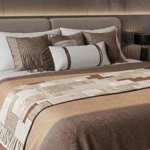 May include: A bed with a neutral color scheme, featuring a beige headboard and a variety of pillows in shades of brown and white. The bed is made with a patterned throw blanket and a fringed edge.