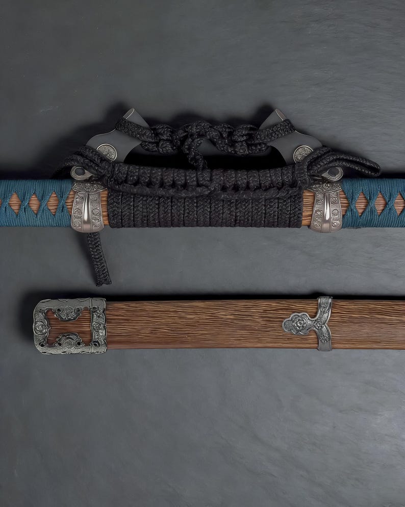 May include: A close-up of a katana sword. The handle is wrapped in black cord, with silver-coloured metal accents. The scabbard is wooden with silver-coloured metal fittings. The blade is partially visible, with a blue and brown pattern.