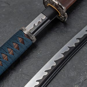 May include: Close-up of a Japanese katana sword. The blade has a wavy pattern, and the handle is wrapped in blue cord. The guard and pommel are ornate metal. The wooden handle is a dark brown colour.