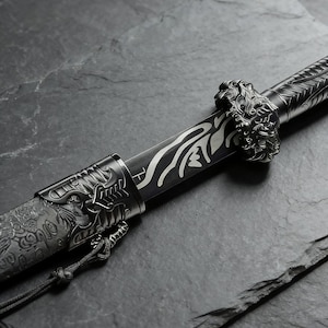 May include: Close-up of a decorative sword with intricate metalwork. The blade features a silver design against a black background. The hilt and scabbard are adorned with detailed carvings, including a lion's head and floral patterns. A black cord is attached.