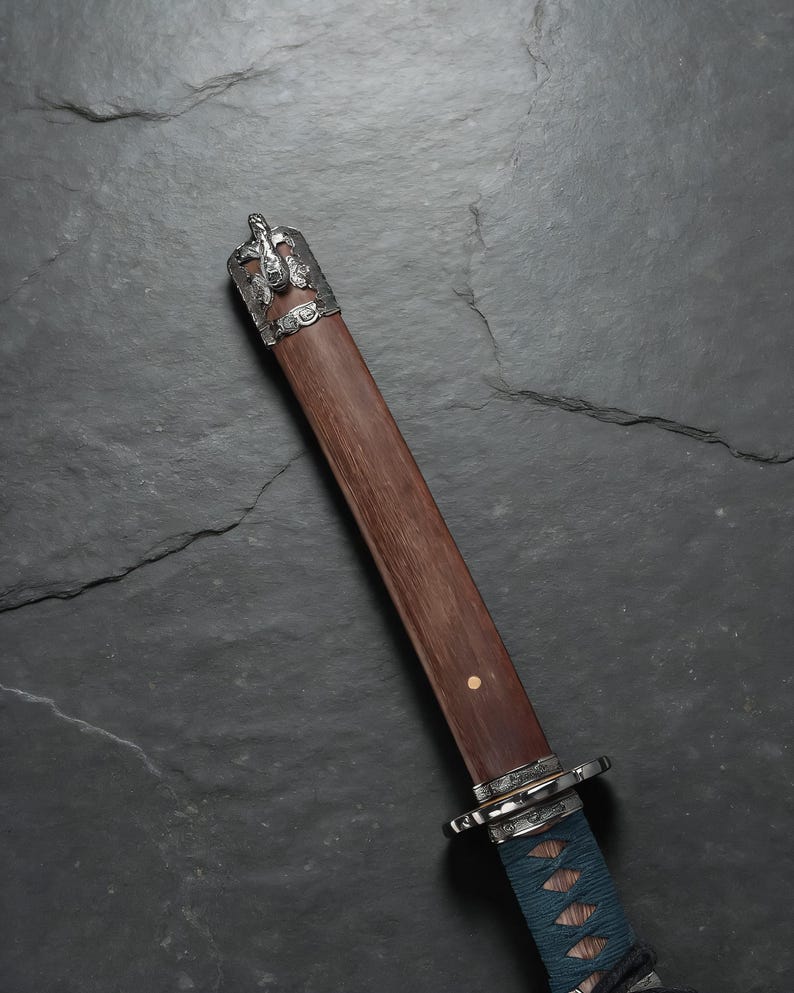 May include: A Japanese katana with a wooden handle and a silver-coloured metal guard. The handle is wrapped in blue fabric. The scabbard is a dark brown colour. The top of the scabbard has a silver-coloured metal cap with a dragon design.