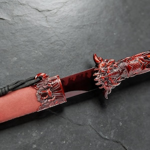 May include: A red decorative dagger with a dragon-themed handle and sheath. The blade has a blood-red finish. The handle and sheath feature intricate dragon carvings. A black cord is attached to the sheath.