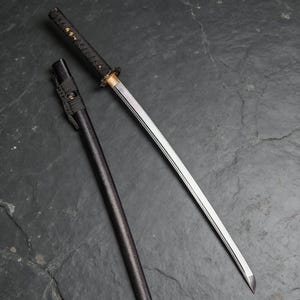 Peut inclure: Un katana japonais avec un manche et un fourreau noirs. La lame est argentée avec une garde dorée. Le manche est enveloppé dans un matériau noir texturé. Le fourreau est cylindrique et également noir.
