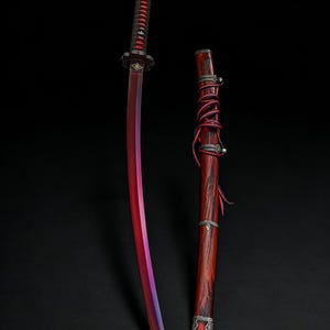 May include: A katana sword with a red and purple blade, a black and red handle, and a wooden scabbard. The scabbard is wrapped with red cord and has silver-coloured accents. The sword is displayed against a black background.