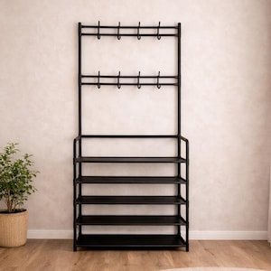 Puede incluir: Una combinación de zapatero y perchero de metal negro. El estante tiene varios estantes para zapatos y ganchos para abrigos. Una pequeña planta en maceta y una alfombra redonda también están en la habitación.