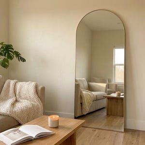 Gold arched full length floor mirror leaning in a cozy living room