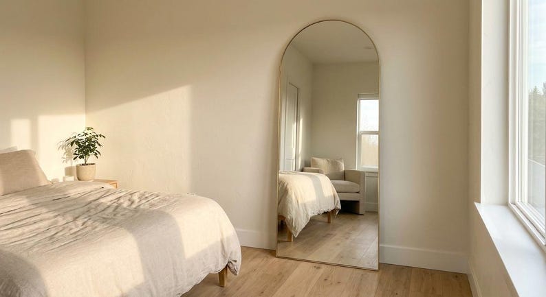 Gold arched full length floor mirror in a bright modern bedroom