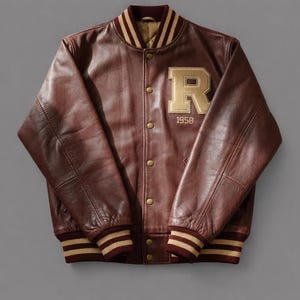May include: A brown leather varsity jacket with a gold "R" patch and the year "1958". The jacket has a ribbed collar, cuffs, and hem with gold and burgundy stripes. It features a button-up front.