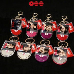 May include: A collection of keychains featuring images of people. Each keychain has a clear, rounded rectangular shape with a metal ring and clasp. The keychains have a red, pink, and purple color scheme, with the text "OSE" on the top.