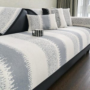 May include: A sofa with a grey, white, and black striped pattern. The sofa has a black leather frame and is adorned with matching throw pillows. A black and white striped mug sits on the sofa.
