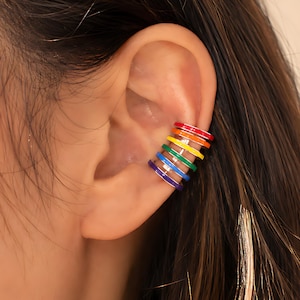 May include: A rainbow-colored ear cuff with red, orange, yellow, green, blue, and purple enamel bands. The cuff is designed to wrap around the ear cartilage. The jewelry is a vibrant accessory.