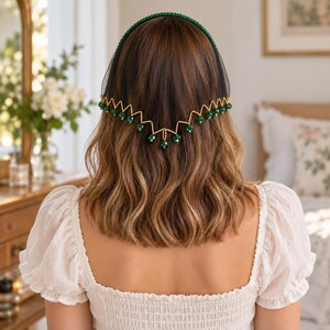May include: A headband featuring a black mesh veil and a gold-toned zigzag wire trim adorned with small, faceted green beads. The headband itself is covered in tiny green beads, creating a cohesive accessory that rests atop the head.