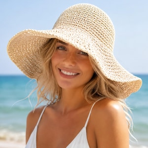 May include: A wide-brimmed straw hat with a natural beige color and a woven texture. The hat features a rounded crown and a flexible, downward-sloping brim that provides coverage. The material is a light-colored, braided straw weave.