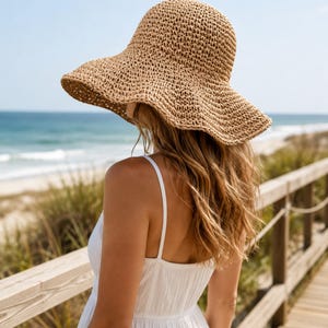 May include: A tan woven straw sun hat with a wide, flexible brim and a rounded crown. The hat features a textured, open-weave pattern throughout the material, providing a lightweight appearance. The brim is slightly wavy and slopes downward.
