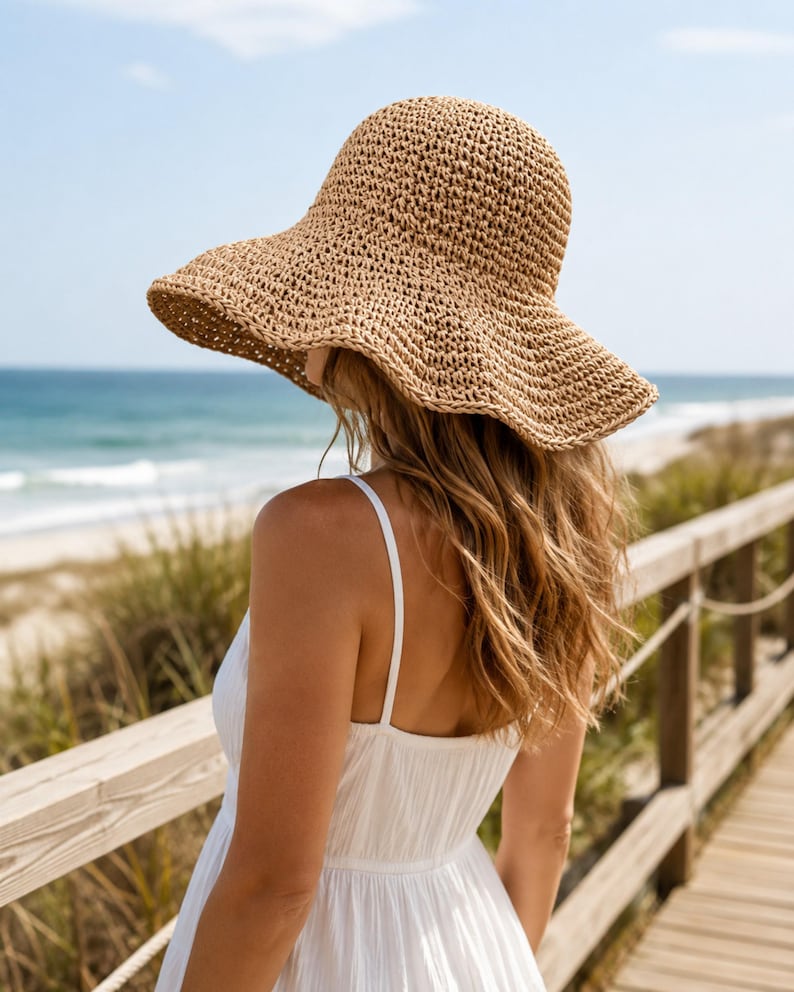 May include: A tan woven straw sun hat with a wide, flexible brim and a rounded crown. The hat features a textured, open-weave pattern throughout the material, providing a lightweight appearance. The brim is slightly wavy and slopes downward.