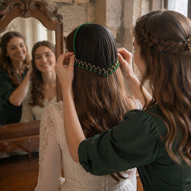May include: A decorative headpiece featuring a black fabric base adorned with a green beaded headband and a gold-toned zigzag trim along the bottom edge, accented with small green beads hanging from each point of the zigzag pattern.