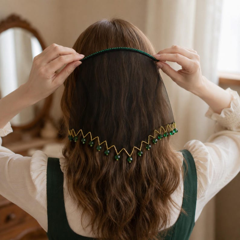 May include: A black sheer veil headband featuring a thin band adorned with small green beads. The lower edge of the veil is trimmed with a gold-toned zigzag pattern, with each point finished with a dangling dark green bead accent.