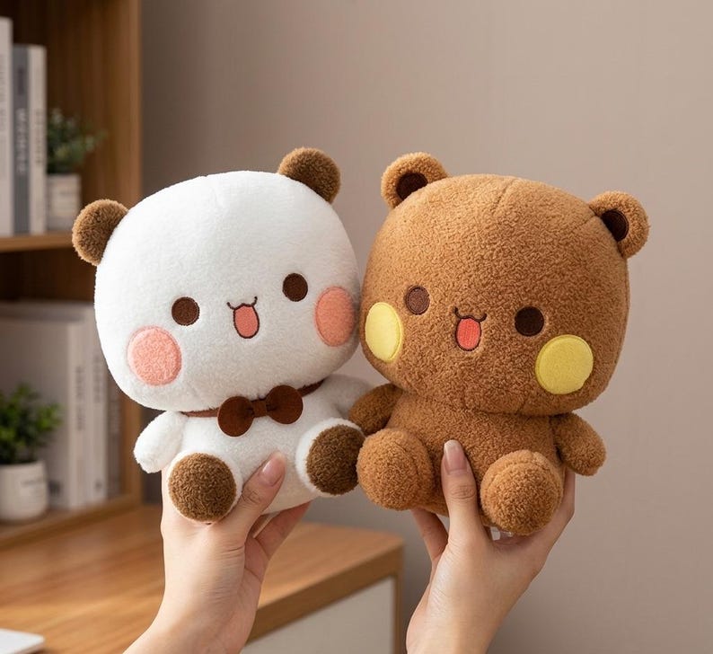 May include: Two plush bear toys. One is white with brown accents and a bow tie, the other is brown with yellow cheek circles. Both have smiling faces with pink cheeks and small tongues.