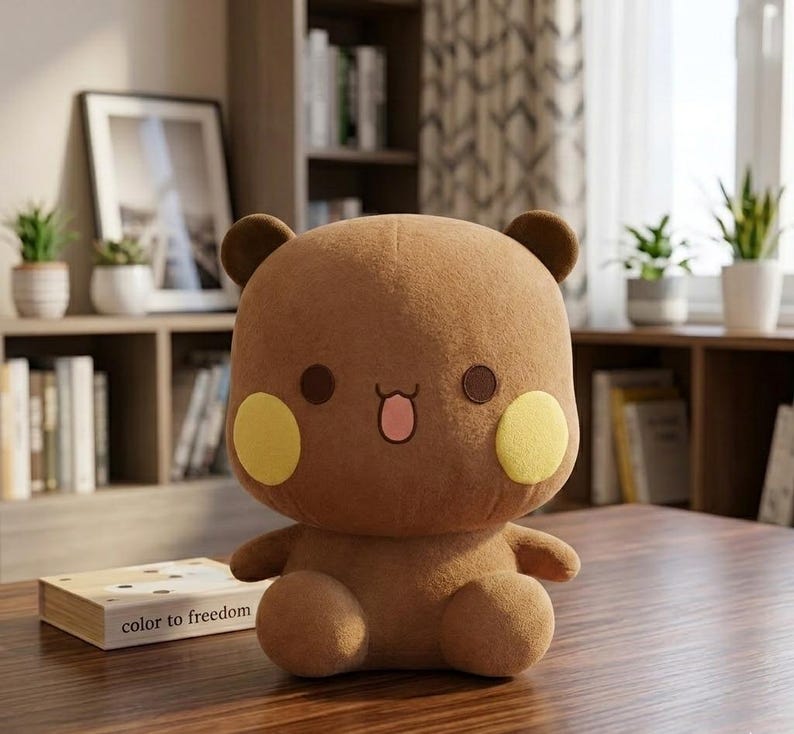 May include: A brown plush bear with yellow cheek circles, brown eyes, and a pink tongue. The bear has small brown ears and is sitting on a wooden surface. A book with the text "color to freedom" is in front of the bear.