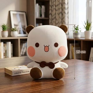 May include: A white plush bear with brown ears, a bow tie, and blush-colored cheeks. The stuffed animal is approximately 10 inches tall. The bear has a cute, cartoonish design and is sitting on a wooden table. The text "color to freedom" is on a book.