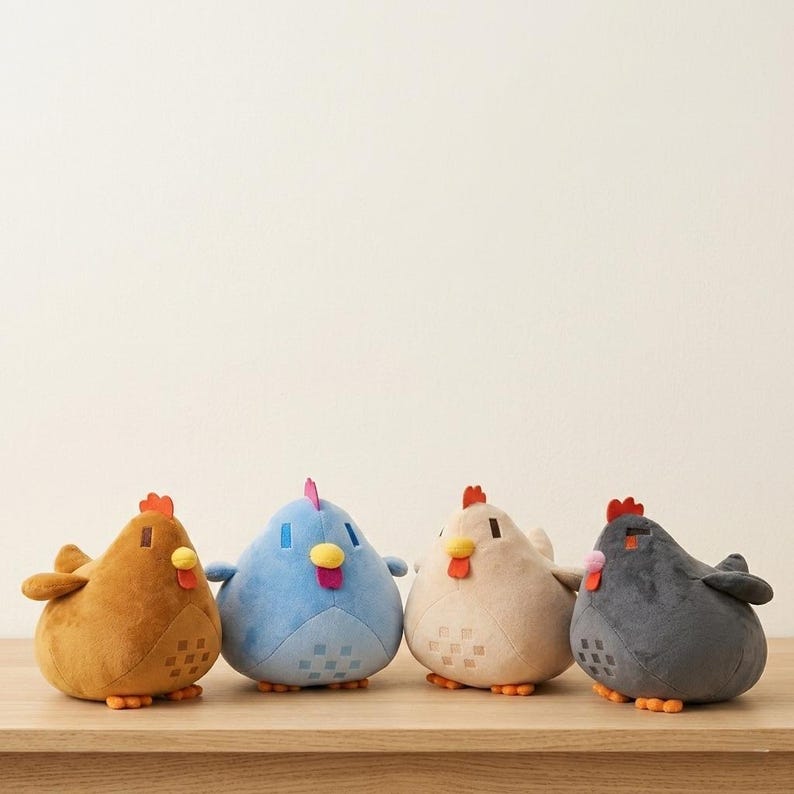 May include: Four plush chicken toys in shades of brown, blue, beige, and gray, each with a red comb and yellow beak. The chickens are sitting on a wooden surface.