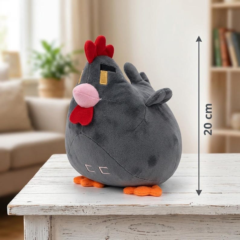 May include: A plush, gray chicken toy with a red comb, wattle, and orange feet. The toy is approximately 8 inches tall. The chicken has a pink beak and small wings. It is sitting on a white table.