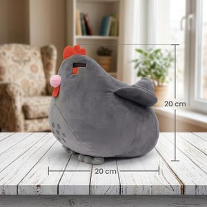 May include: A gray plush chicken toy, approximately 8 inches in length and height. The chicken has a red comb, a pink wattle, and a pixelated design. It is sitting on a white wooden surface.