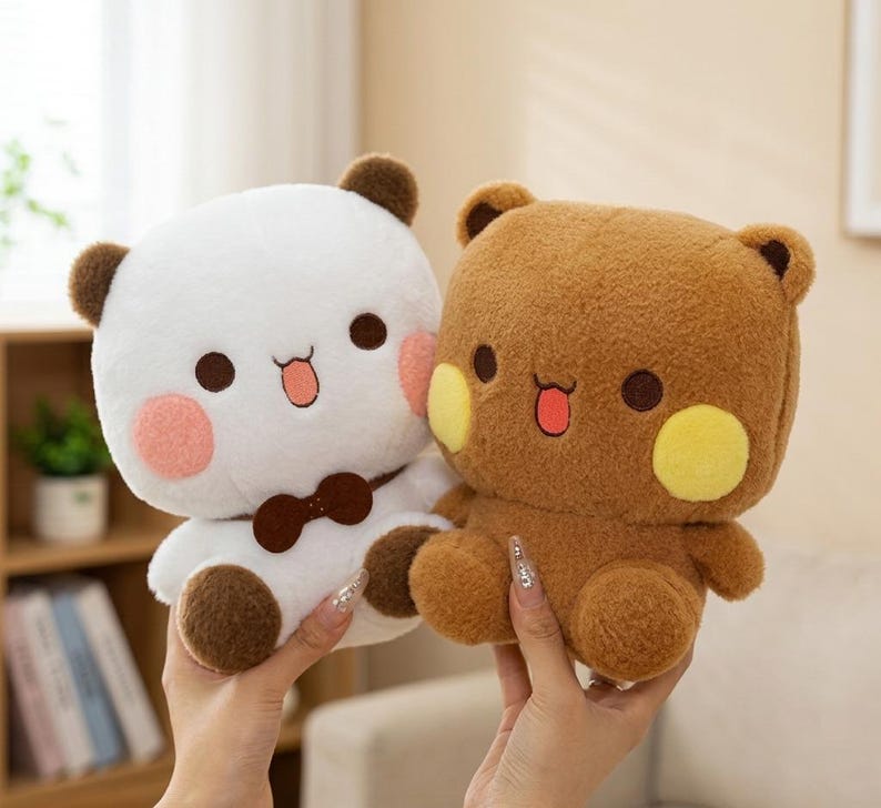 May include: Two plush bear toys. One is white with brown ears, a brown bow tie, and pink cheeks. The other is brown with yellow cheeks. Both have black eyes and open mouths with red tongues. The toys are held up by hands.