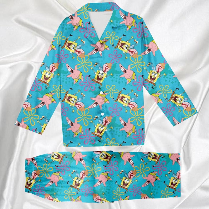 Op de afbeelding: Een tweedelige pyjamaset met een lichtblauwe achtergrond en een herhaald patroon van SpongeBob SquarePants, Patrick Star en bloemmotieven. De top met lange mouwen heeft een kraag en een knoopsluiting. De bijpassende broek maakt de set compleet.