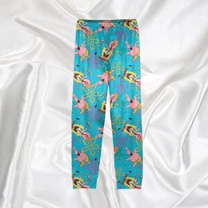Op de afbeelding: Blauwe pyjamabroek met een herhalend patroon van SpongeBob SquarePants, Patrick Star en bloemmotieven. De broek heeft een elastische tailleband en is gemaakt van een zacht, comfortabel materiaal. De pyjamabroek is ontworpen voor nachtkleding.