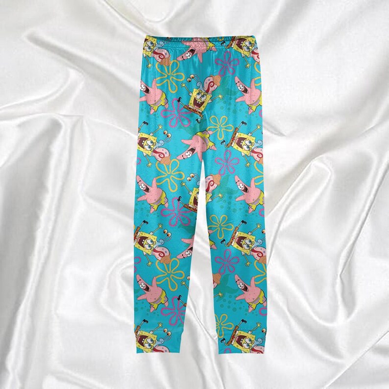 Op de afbeelding: Blauwe pyjamabroek met een herhalend patroon van SpongeBob SquarePants, Patrick Star en bloemmotieven. De broek heeft een elastische tailleband en is gemaakt van een zacht, comfortabel materiaal. De pyjamabroek is ontworpen voor nachtkleding.