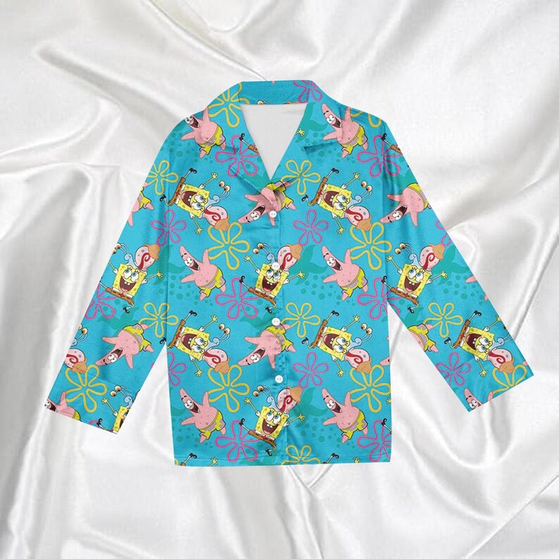 Op de afbeelding: Turquoise pyjamashirt met knopen, met een herhaald patroon van de tekenfilmfiguren SpongeBob SquarePants en Patrick Star. Het shirt met lange mouwen heeft een klassieke kraag en een knoopsluiting.