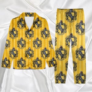 May include: Yellow pajama set with a repeating pattern of a black and gray crest on a striped background. The set includes a button-down shirt and matching pants. The crest features a badger.