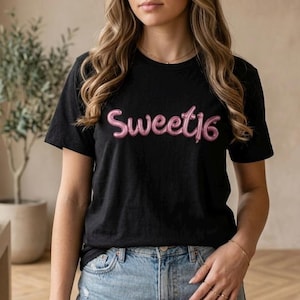 May include: Black t-shirt with the text "Sweet 16" in pink, balloon-style lettering. The shirt is worn with blue jeans. The image is taken indoors, with a neutral background and a plant in a pot.
