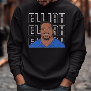 May include: Black sweatshirt featuring a graphic of a smiling person in a blue shirt, with the name "ELLIJAH" stacked three times in white block letters. The design is centered on the front of the sweatshirt.
