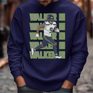 May include: Navy blue sweatshirt featuring a football player graphic. The player is wearing a white and blue uniform with the number 9. The name "WALKER" is printed in green, stacked vertically on the sweatshirt.