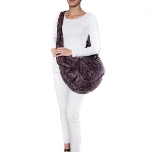 May include: A large, dark purple shoulder bag with a snakeskin pattern. The bag is worn over the shoulder and is paired with a white long-sleeve shirt and white pants. The person is wearing black heeled sandals.