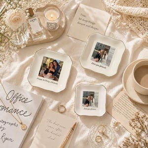 Puede incluir: Una colecci&oacute;n de bandejas decorativas de cer&aacute;mica blanca con ribete dorado, cada una con una fotograf&iacute;a. Una bandeja tiene el texto "Happy birthday Adelaide", y otras dos dicen "Love you forever". La escena incluye una vela, perfume y joyas.
