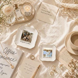 Puede incluir: Una variedad de elementos decorativos dispuestos sobre una superficie color crema. Incluye dos platos cuadrados con fotos familiares, un frasco de perfume, una vela encendida, una taza de caf&eacute;, joyas y notas manuscritas con texto. El texto en los platos dice "Family love is endless" y "There's no place like home."